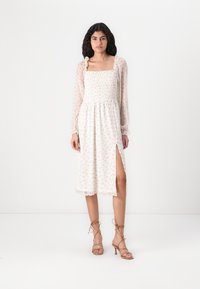 Rochie ușoară, cu imprimeu floral, cu un corp strâns, mâneci lungi transparente, fante laterale și tiv în formă de val. Sandale cu curele completează aspectul.