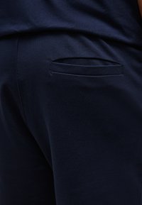 Κοντινό πλάνο σκούρων μπλε παντελονιών από ύφασμα με οριζόντια πίσω τσέπη με σχισμή και λεπτές ραφές.