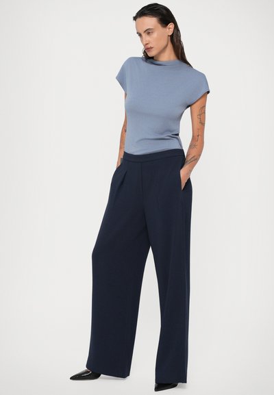 Blusa de manga curta azul clara com gola alta, combinada com calças largas azul marinho com pregas frontais e bolsos laterais.