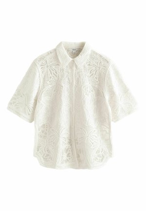 Blouse blanche à manches courtes en dentelle avec motifs floraux et feuilles, boutonnée devant, avec un col pointu.