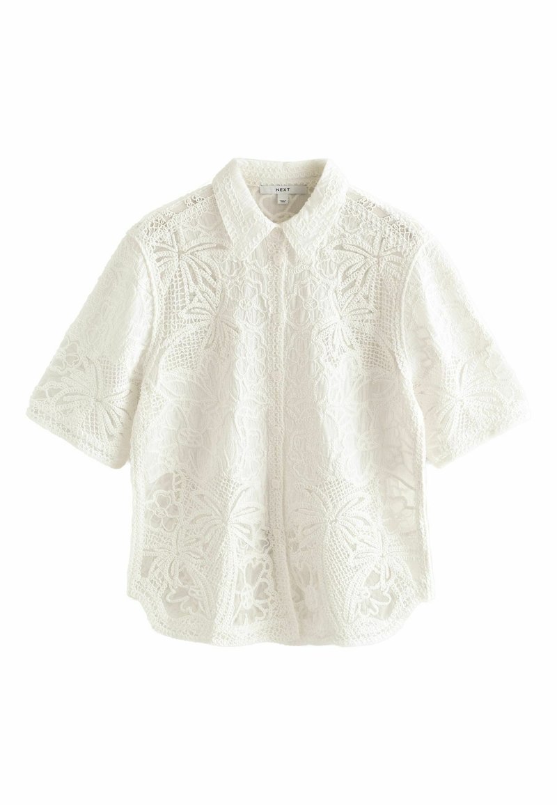 Blouse blanche à manches courtes en dentelle avec motifs floraux et feuilles, boutonnée devant, avec un col pointu.