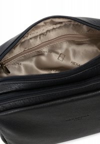 Pochette in pelle nera con apertura a zip, fodera interna beige con un motivo ripetuto "HEXA" e una tasca interna con zip.