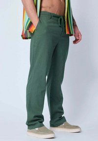 Pantalons verts amples en tissu léger, dotés d'une taille élastique avec cordon de serrage. Assortis à des chaussures beiges à enfiler.