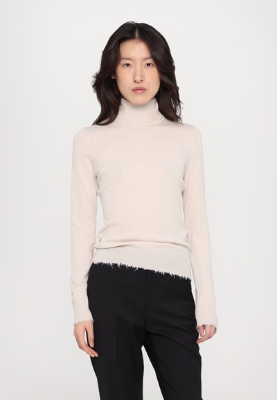 Beige turtleneck sweater with long sleeves, featuring a frayed hem and cuffs, made of a soft knitted material. Paired with black trousers.