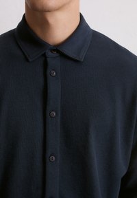Camicia color blu navy con colletto realizzata in tessuto testurizzato, con chiusura a bottone e bottoni scuri, e colletto strutturato.