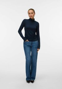 Mørkeblå turtleneck-top lavet af glat stof parret med lys blå flare jeans. Outfittet har en tætsiddende pasform og lange ærmer.