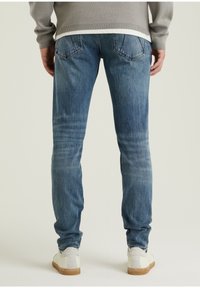 Jeans de denim azul desgastado con un corte ajustado, que presentan bolsillos traseros con parche y detalles de costura mínimos, combinados con zapatillas blancas.