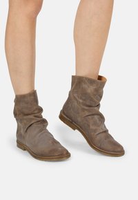 Botas de cuero marrón hasta el tobillo con un diseño suelto, textura suave y una puntera redonda minimalista; presentan una suela plana marrón.