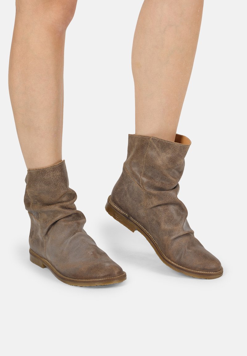 Botas de cuero marrón hasta el tobillo con un diseño suelto, textura suave y una puntera redonda minimalista; presentan una suela plana marrón.