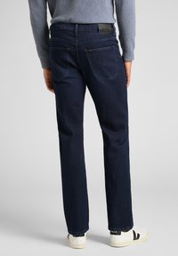 Mörkblå denimjeans med rak ben, som har två bakfickor, diskret sömnad och en svart läderetikett i midjan.