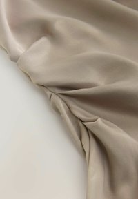 Beige satiinikankaat, jossa on sileä pinta, esittelee kiertyneen osan, joka luo pehmeitä laskoksia ja hienostunutta kiiltoa.