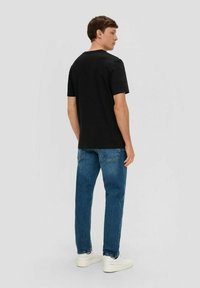 Schwarzes Baumwoll-T-Shirt mit rundem Halsausschnitt, kombiniert mit hellblauen Jeans. Glatte Textur, lässige Passform und weiße Sneaker.