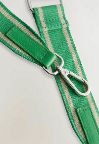 Grüner gewebter Gürtel mit cremefarbenen Streifen, ausgestattet mit einem grünen Lederakzent und einem silbernen Metallclip zum Befestigen. Sichtbare strukturierte Oberflächendetails.