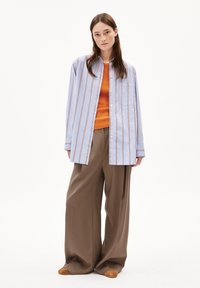 Lichtblauw gestreepte overhemden met lange mouwen, gecombineerd met een oranje aangesloten top en losse bruine broeken, gedragen met bruine schoenen.