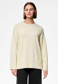 Licht beige oversized sweater met ribgebreide mouwen en zoom, ronde hals en zachte textuur. Combineert goed met donkere broek voor contrast.