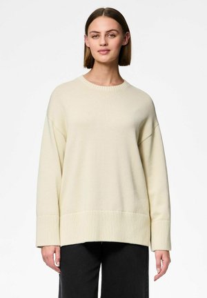 Jasno beżowy, oversize sweter z prążkowanymi mankietami i dołem, okrągłym dekoltem oraz miękką teksturą. Dobrze komponuje się z ciemnymi spodniami, tworząc kontrast.