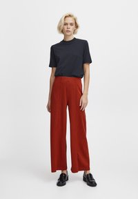 Haut noir à manches courtes, pantalon à carreaux rouge à jambes larges et mocassins noirs. Design simple, tissu doux et coupe décontractée tout au long.