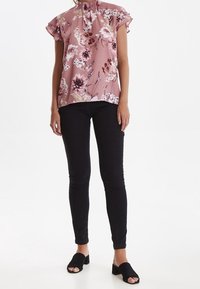 Blusa floreale rosa con maniche a volant, abbinata a jeans skinny neri e scarpe slip-on nere. Tessuto morbido, motivo floreale dettagliato.