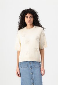 Crème korte mouwen sweater met textuur bloemenborduursel, ronde halslijn en ribbelzoom, gedragen met een denim rok met knoopdetails.