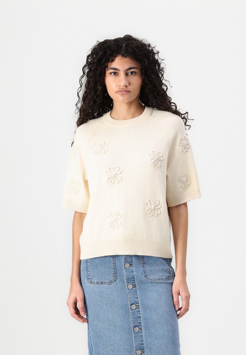 Crème korte mouwen sweater met textuur bloemenborduursel, ronde halslijn en ribbelzoom, gedragen met een denim rok met knoopdetails.