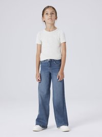 T-shirt gris clair à manches courtes, jean en denim bleu à jambes larges, et baskets blanches. Tissu lisse, coupe décontractée, et design à jambes droites.