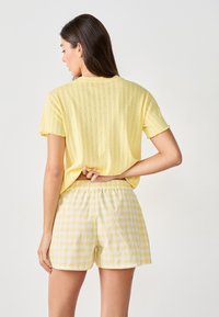 Camisa amarilla de manga corta con textura y dobladillo en forma de ondas, combinada con pantalones cortos sueltos de cuadros gales amarillos y blancos con cintura elástica.