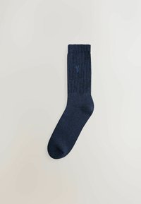 En enkelt marineblå sok med ribbet overdel og et lille rådyrlogo broderet på siden, liggende fladt på en lys baggrund.