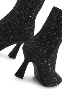 Botines negros con una superficie texturizada decorada con tachuelas brillantes. Los tacones son cortos y acampanados, realzando el diseño moderno.