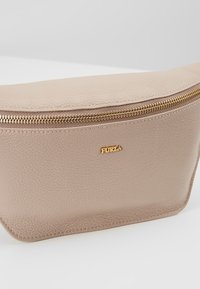 Pochette en cuir beige texturé avec une fermeture éclair dorée et un petit logo Furla doré à l'avant, sur fond blanc uni.