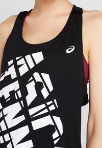 Černý top bez rukávů s bílým geometrickým grafickým designem, kulatým výstřihem a bez rukávů. Nositý s vínovým sportovním podprsenkovým stylem pod ním.