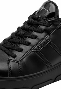 Sneaker nera con lacci, realizzata in pelle sintetica, con texture liscia, punta rotonda e suola in gomma nera testurizzata. Presenta un dettaglio del logo sul lato.