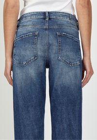Högmidjade blå denimjeans med en lätt blekning, med två bakfickor och en ren finish längs midjebandet och sömmarna.