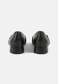 Chaussures en cuir noir avec une finition lisse et élégante, bout arrondi, petit talon et accents décoratifs sur les côtés.