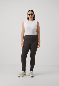Black stretchy leggings and a white sleeveless top, paired with gray and yellow sneakers and dark sunglasses, against a plain background.