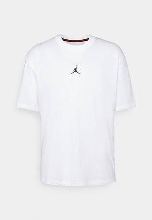 Camiseta blanca de algodón con un logo negro de Jordan en el pecho, cuello redondo con rayas rojas y negras, y mangas cortas.