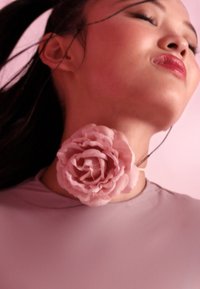 Accesorio para el cuello que presenta una gran rosa de tela texturizada en color rosa, unida a una parte superior de tonalidad clara, con un fondo de piel suave.