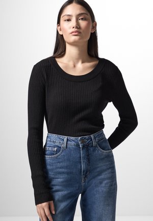 Haut noir à manches longues côtelé avec un large décolleté, associé à un jean en denim bleu taille haute avec une fermeture à bouton et des poches avant.