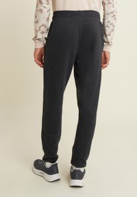 Pantaloni della tuta neri con una vestibilità rilassata, vita elastica e superficie liscia, abbinati a scarpe da ginnastica scure.