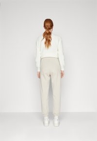 Hvit teksturert genser med en kort design, sammen med beige joggebukser med elastisk midje og hvite sneakers, sett fra baksiden.