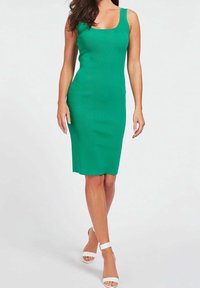 Robe verte côtelée à silhouette ajustée, avec un décolleté carré et des bretelles épaisses. Portée avec des talons blancs à brides pour un contraste.