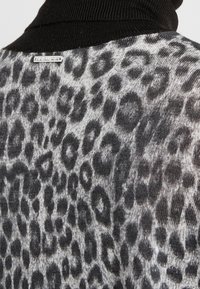 Sweter w leoparda z miękką, szarą bazą z czarnymi plamami, prążkowanym czarnym golfem i małą metalową metką marki.