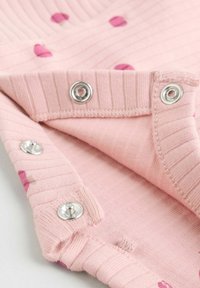 Rosa gerippter Stoff mit teilweise geöffneten Druckknöpfen, der das weiche Innenfutter und kleine florale Musterdetails zeigt.