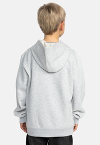 Grijze hoodie met een losse pasvorm, voorzien van een grote capuchon en geribde manchetten. De binnenkant heeft een contrasterende textuur, zacht tegen de huid.