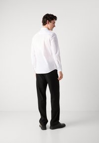 White long-sleeve shirt with a curved hem, paired with black straight-leg trousers. The shoes are black and flat. Minimalist design.