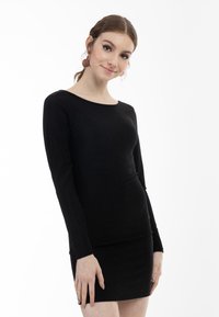 Schwarzes Langarmoberteil mit rundem Halsausschnitt, taillierter Silhouette und weicher Textur, kombiniert mit einem passenden schwarzen Bodycon-Rock.