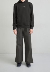 Felpa nera con cappuccio e tasca frontale, abbinata a pantaloni grigio scuro a gamba larga. Entrambi i capi hanno una texture liscia.