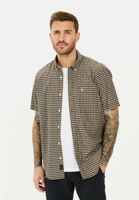 Kurzärmliges kariertes Hemd in Braun und Schwarz, mit Button-Down-Kragen und weißen Knöpfen, über einem weißen T-Shirt getragen.