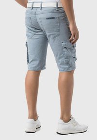 Shorts cargo à rayures bleues et blanches avec poches, passants de ceinture et un design ajusté, portés avec des baskets blanches. Matière en coton texturé.