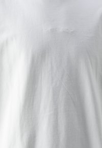 Weißes Baumwoll-T-Shirt mit dezent geprägtem Logo. Der Stoff wirkt weich mit einer leicht zerknitterten Textur und hat ein rundes Halsdesign.