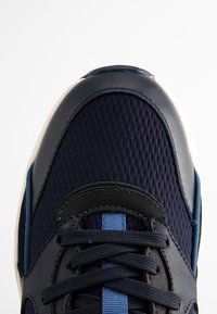 Navy mesh sneaker with smooth leather accents, rounded toe, flat black laces, and a textured pattern on the upper.